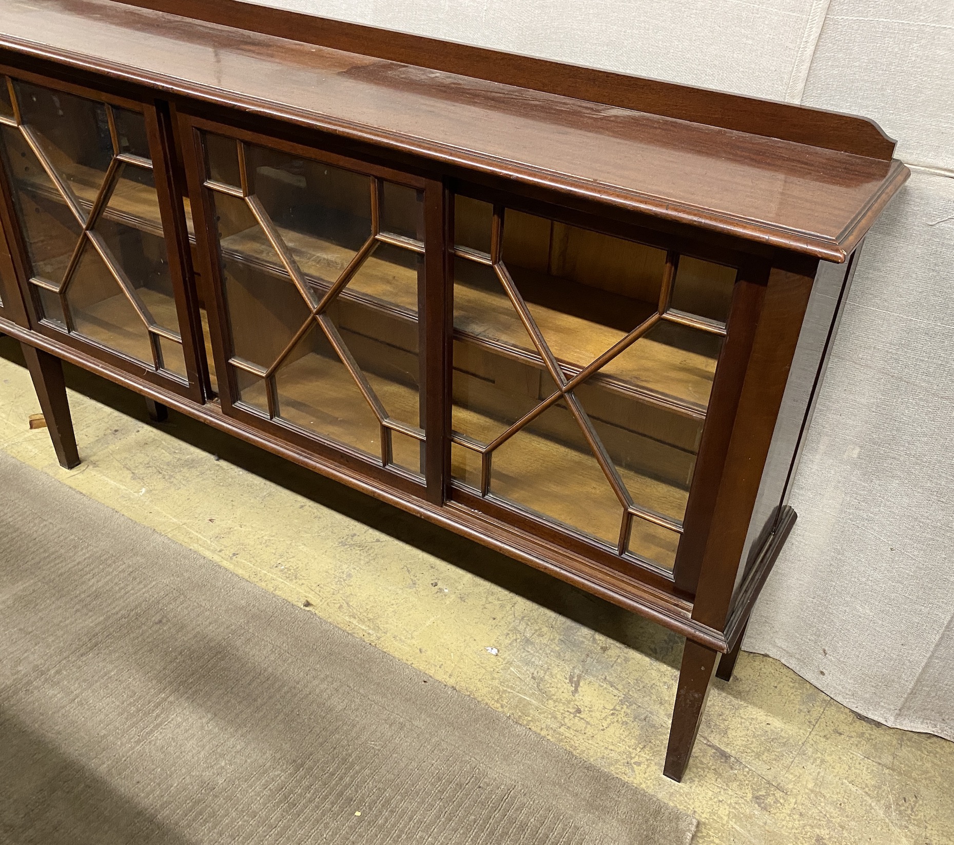 An Edwardian glazed mahogany dwarf bookcase, enclosed by six astragal glazed sliding doors, width 290cm, depth 34cm, height 94cm